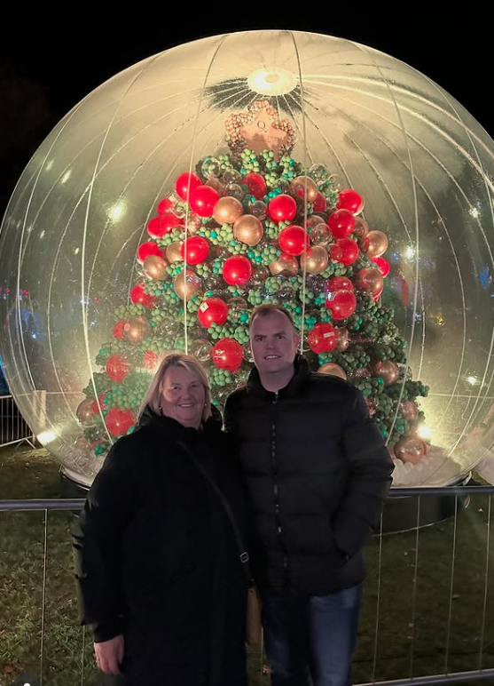 Pár pred veľkou vianočnou guľou s ozdobeným stromom vo vnútri, osvetlenou v noci.