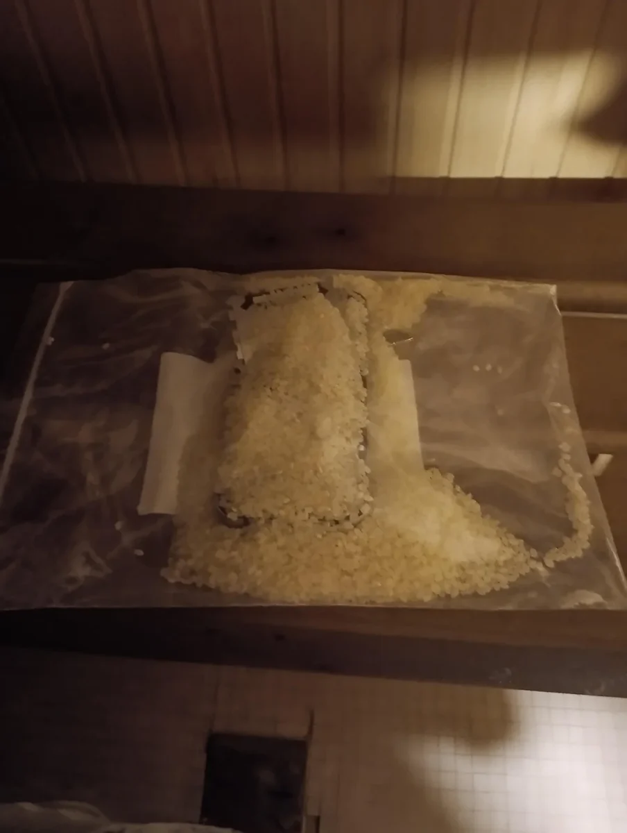 Telefón v plastovom sáčku s ryžou na drevenom povrchu, sušenie od vlhkosti.