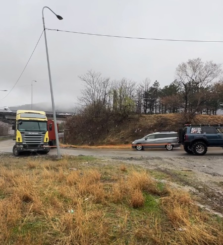 Kamión a autá zaparkované vedľa cesty v jesennom prostredí s holými stromami a oblačnou oblohou.