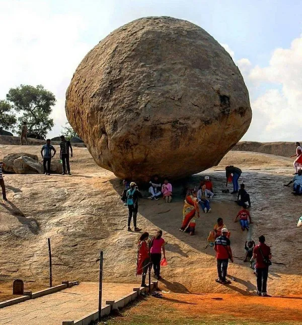Veľký balvan na svahu obklopený ľuďmi, ktorí ho obdivujú a fotografujú pod jasnou oblohou.