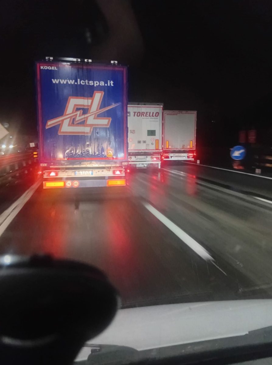 Tri kamióny na nočnej diaľnici, mokrá cesta, červené zadné svetlá, bezpečný odstup.