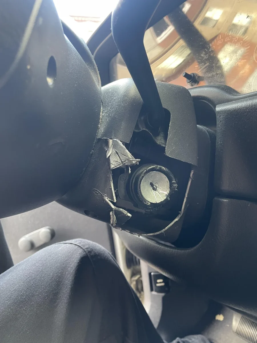 Rozbitý plastový kryt pod volantom auta, odhaľujúci poškodený zapaľovací spínač.