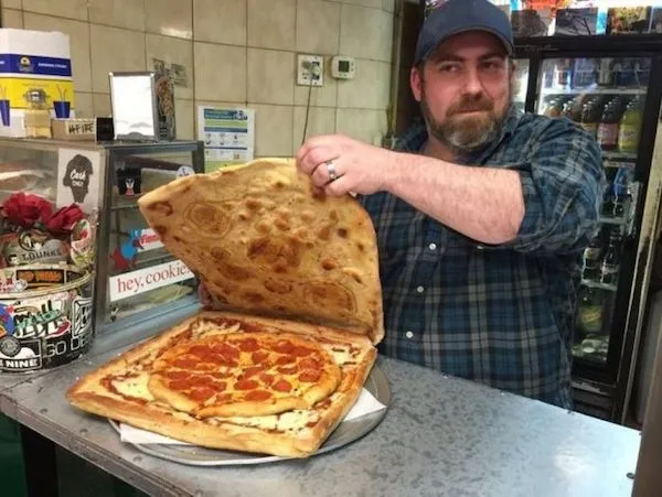 Muž ukazuje špeciálnu pizzu zabalenú v obrovskej placke v reštaurácii. Pizza s pepperoni na kovovej doske.