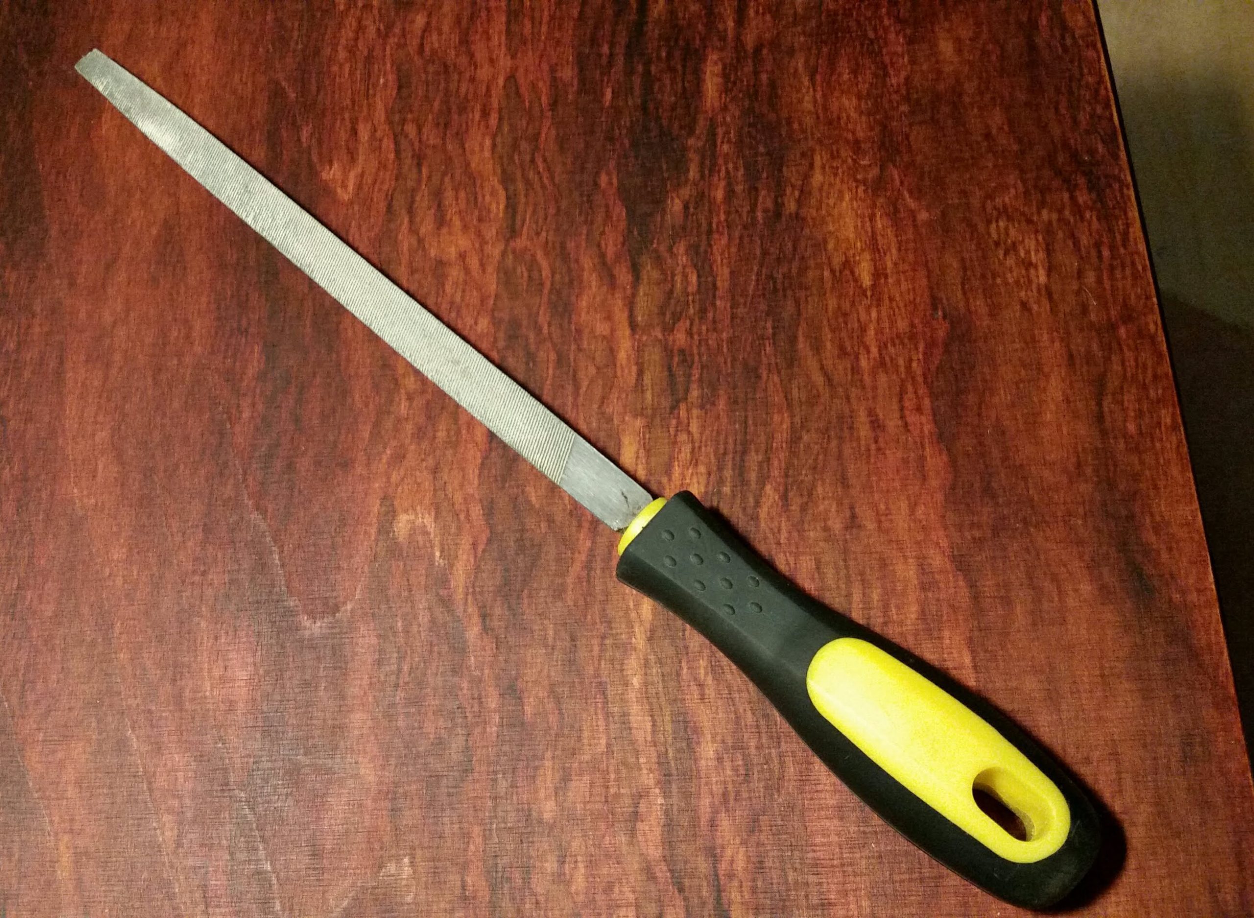 Ručná pilník s čierno-žltou rukoväťou na drevenom povrchu. Praktický nástroj na údržbu a opravy.