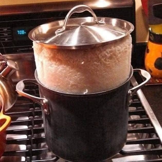 Hrniec s varom pretekajúcej ryže na sporáku, nedbanlivé varenie.