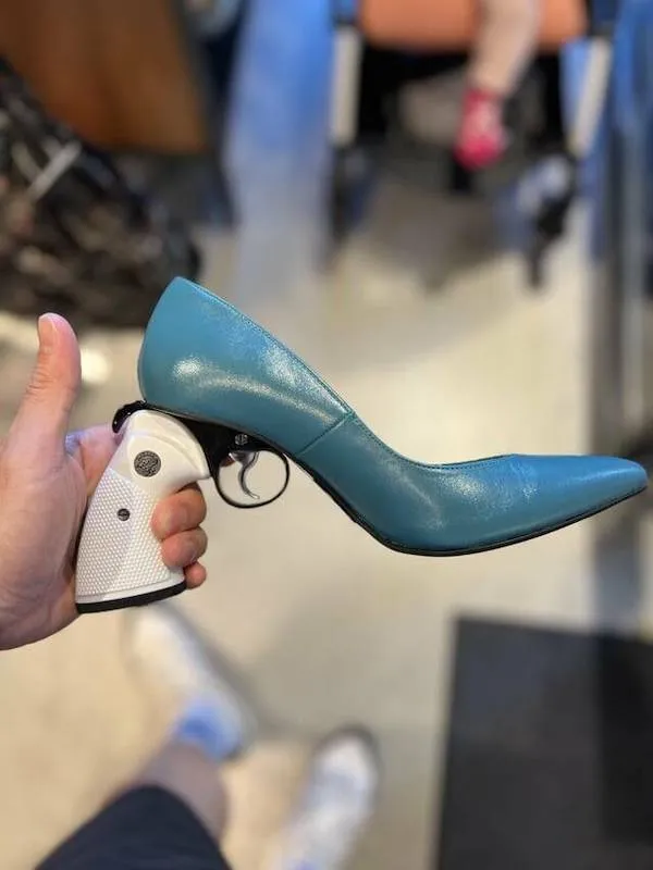 Muž drží zbraň prerobenú na modrú ženskú topánku, kreatívny dizajn.