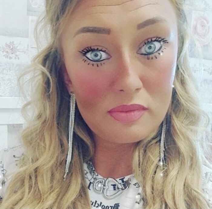 Žena s výrazným líčením a dlhými blond vlasmi nosí trblietavé náušnice, portrét.