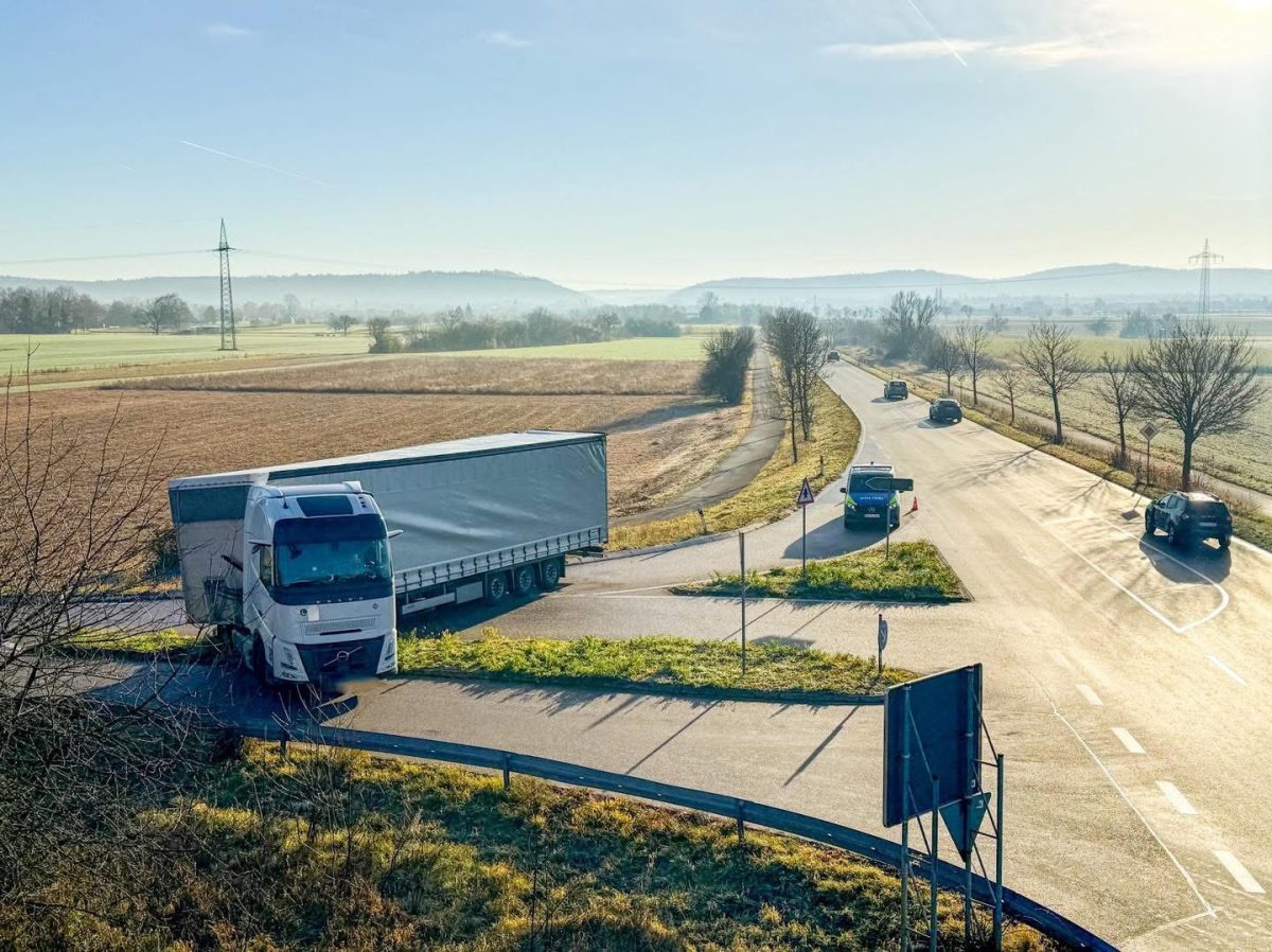 Kamión na úzkej vidieckej križovatke so slnečným počasím na pozadí.