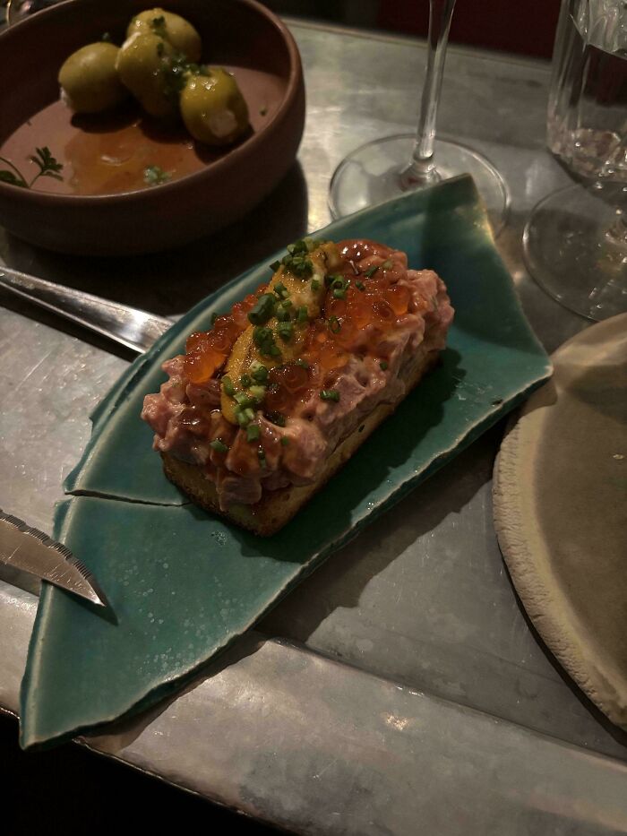 Gastronomická delikatesa: Chlieb s lahodnou nátierkou, lososovým kaviárom a bylinkami, podávaný na umeleckom tanieri.