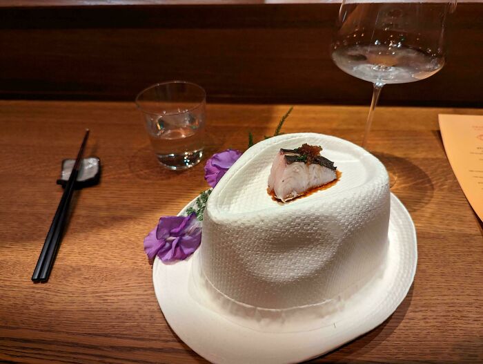 Elegantne podávané sushi na klobúku dekorované kvetinami, servírované s nápojmi na drevenom stole.