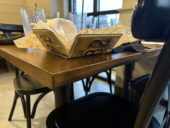 Stôl v reštaurácii s pohármi a miskou z poznávacej značky plnou papierových obrúskov.