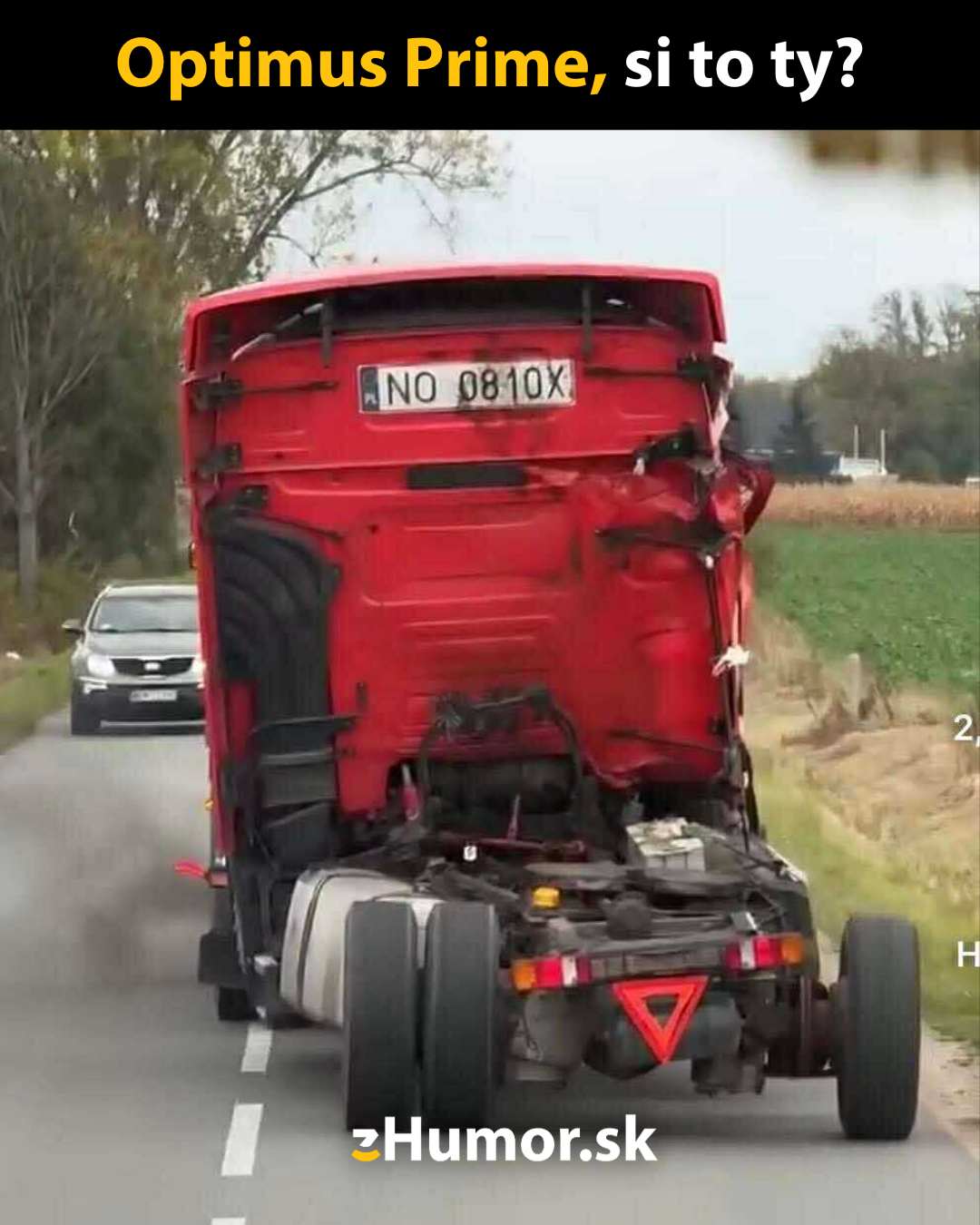 Červený kamión bez prívesu s preklopenou kabínou na vidieckej ceste, vtipný text nad ním.