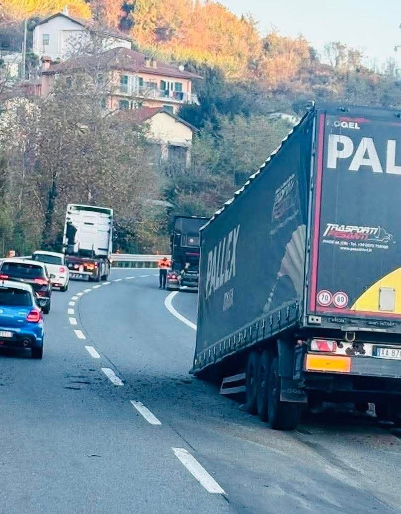 Kamión uviaznutý pri ceste, obklopený kopcovitým terénom a autami na frekventovanej ceste.