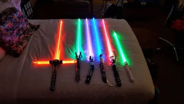 Rôznofarebné svetelné meče rozložené na posteli v tmavej miestnosti.
