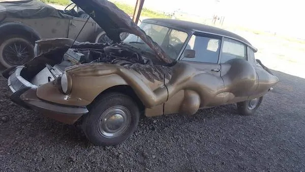 Staré, zdeformované auto s otvorenou kapotou na štrkovom podlaží v garáži.