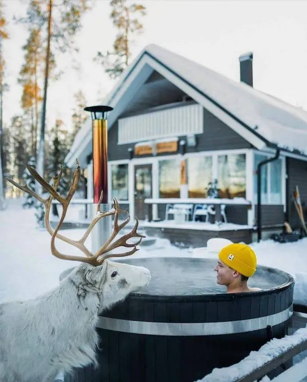 Muž v žltej čiapke v kúpeli na dvore zasneženého domu s pozorujúcim sobom.
