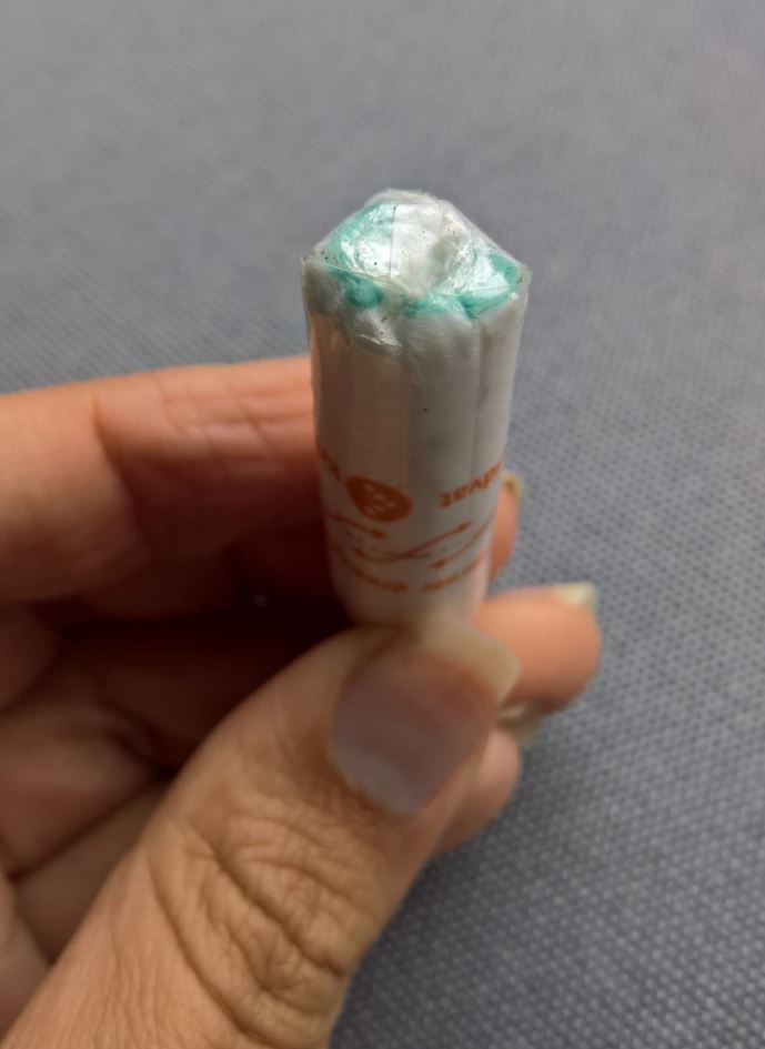 Niekto drží bielu tyčinku na šedej textílii, detailný záber na ruke a prstoch.