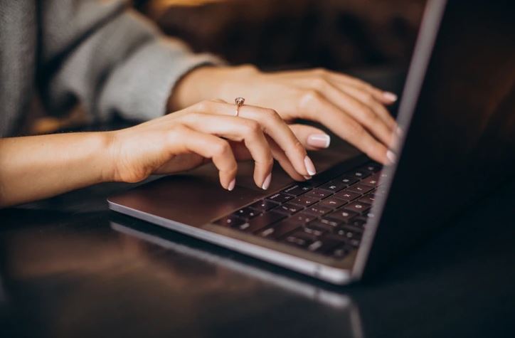 Osoba píšuca na laptopu, detail prstov na klávesnici pri práci v interiéri.