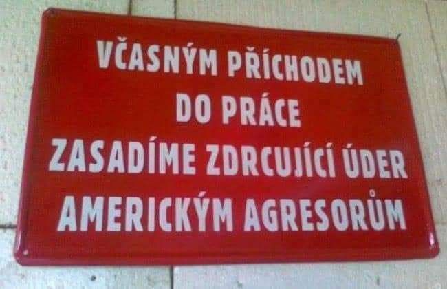 Červená tabuľa s nápisom: Včasným příchodem do práce zasadíme zdrcující úder americkým agresorům.