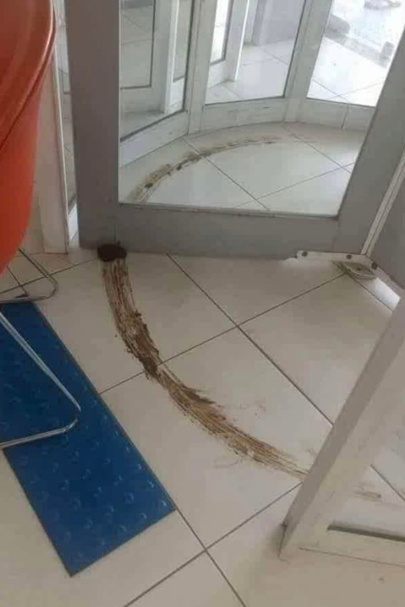 Špinavá stopa na bielych dlaždiciach pri otočných dverách - dôkaz potreby údržby vo vstupnej hale.