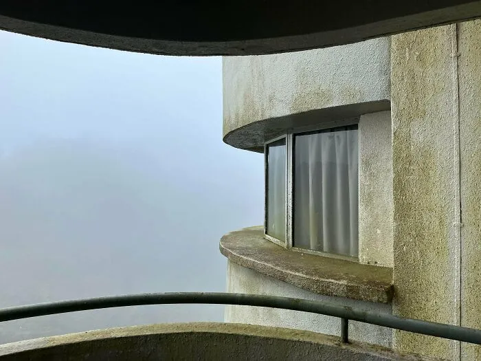 Zakalený výhľad z balkóna s modernou architektúrou a zaoblenými stenami, obklopený hmlou.