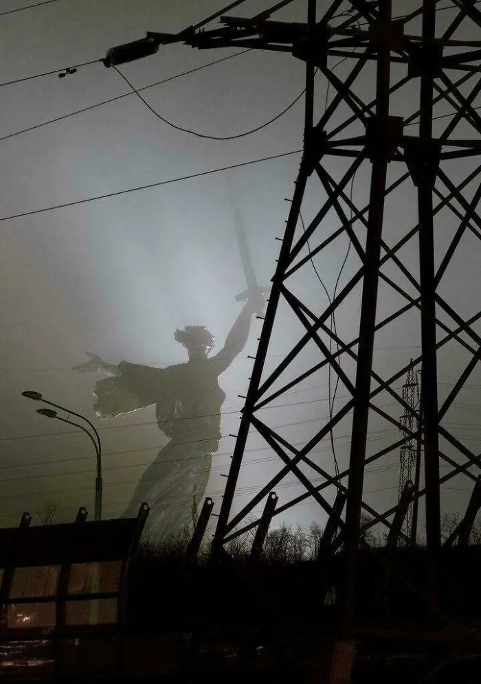 Záhadný pohľad na sochu v hmle za elektrickým stĺpom, symbolizujúci kontrast medzi umením a priemyslom.