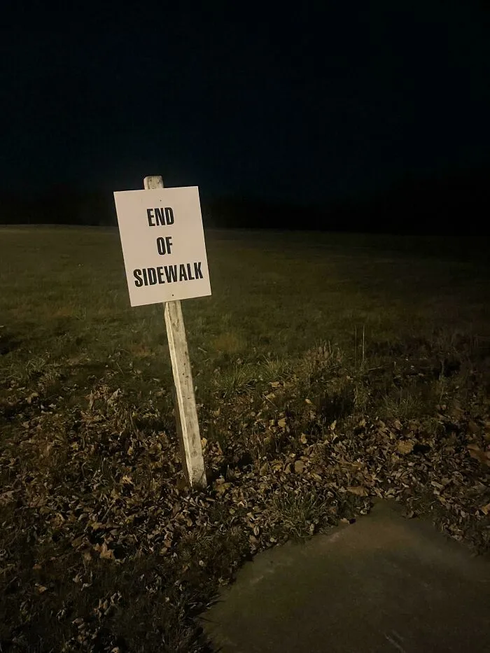 Značka Koniec chodníka na tmavej lúke, mraky a tráva v pozadí pod nočnou oblohou.