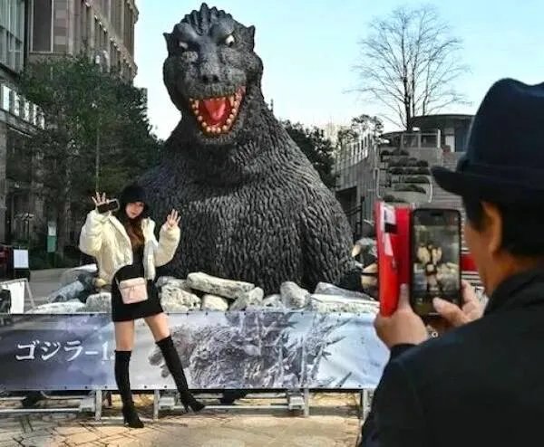 Žena pózuje pred obrovskou sochou Godzilly, zatiaľ čo ju niekto fotografuje na ulici mesta.