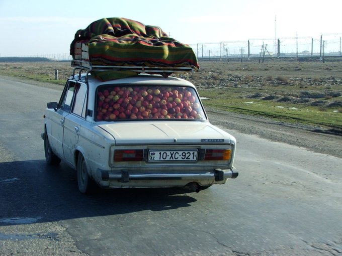 Auto plne naložené jablkami a nákladom na streche, jazdiace po opustenej vidieckej ceste.
