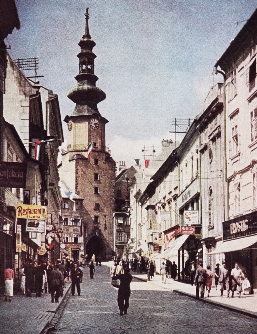 Historická bratislavská ulica s Michalskou bránou, obchodmi a chodcami v mestskom ruchu.