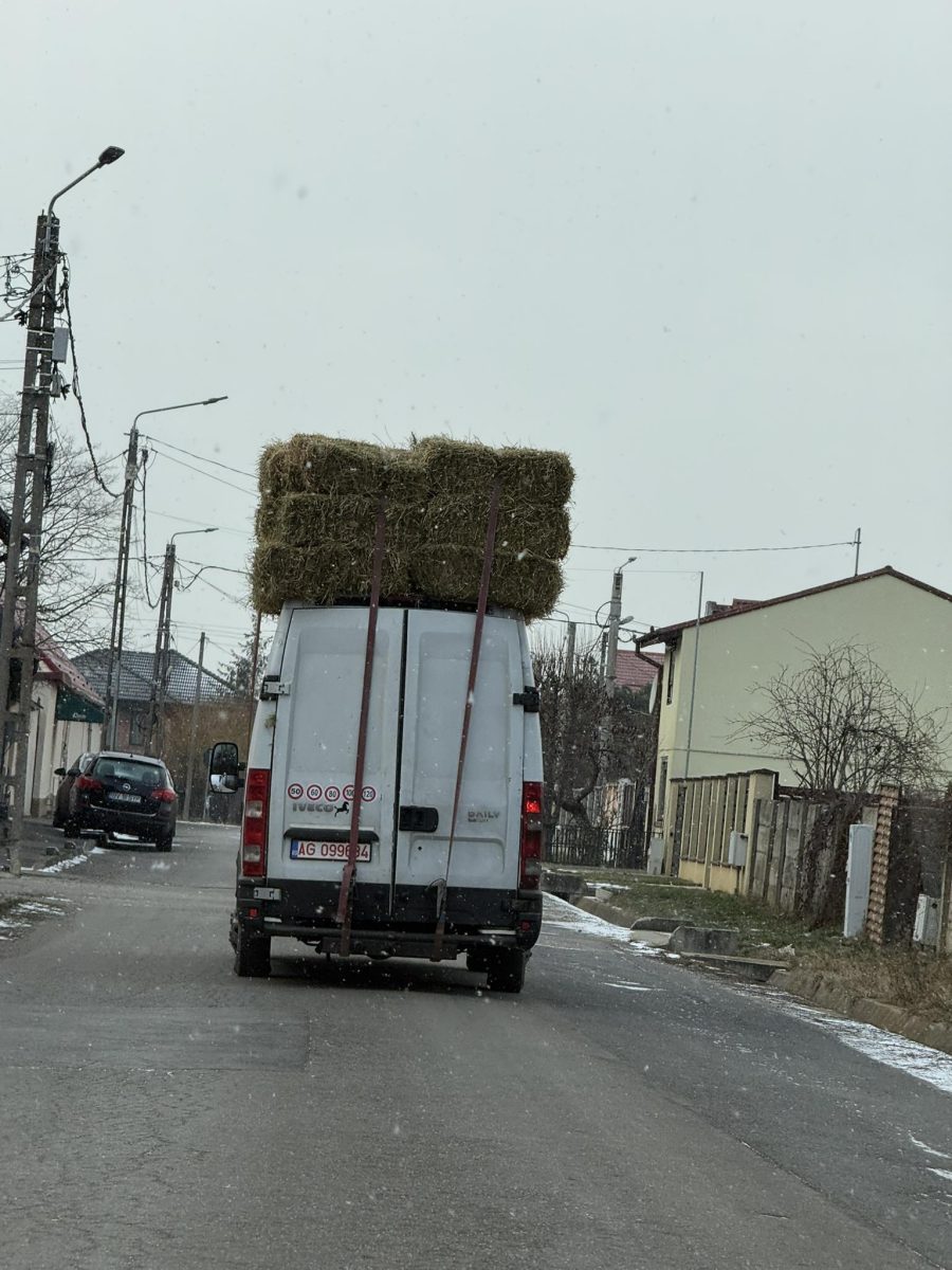 Dodávka s balíkmi sena na streche jazdí po zasneženej dedinskej ceste.