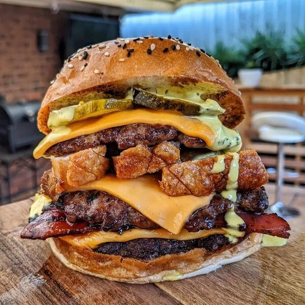 Šťavnatý cheeseburger s dvoma plátkami syra, slaninou, bravčovým mäsom a kyslou uhorkou na drevenej doske.