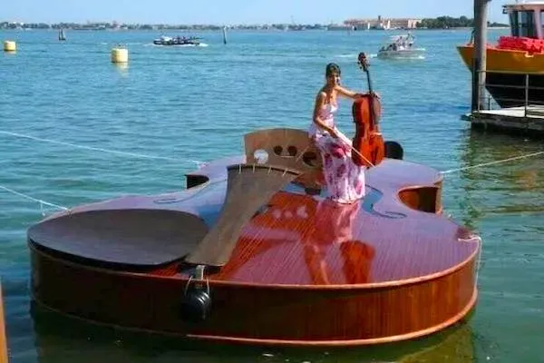 Loď v tvare huslí s muzikantkou na palube na jazere, krásny slnečný deň.
