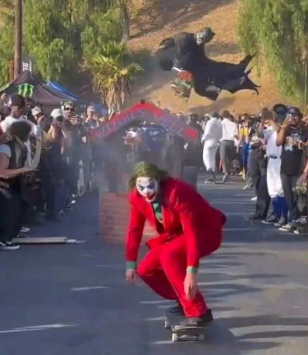 Klaun na skateboarde prechádza dráhou plnou fanúšikov na kostýmovanej akcii.
