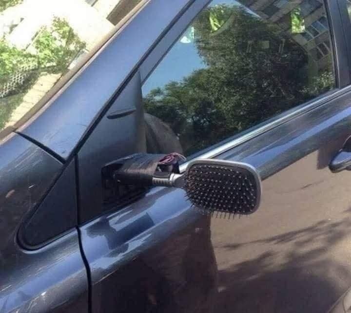 Auto so spätným zrkadlom nahradeným hrebeňom, kreatívna oprava zrkadla na modrom aute.