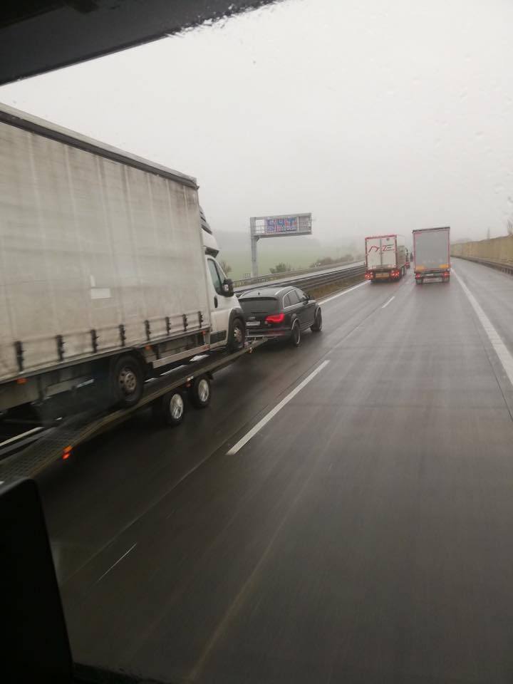 Osobné auto ťahá nákladný príves s dodávkou na diaľnici v daždivom počasí.