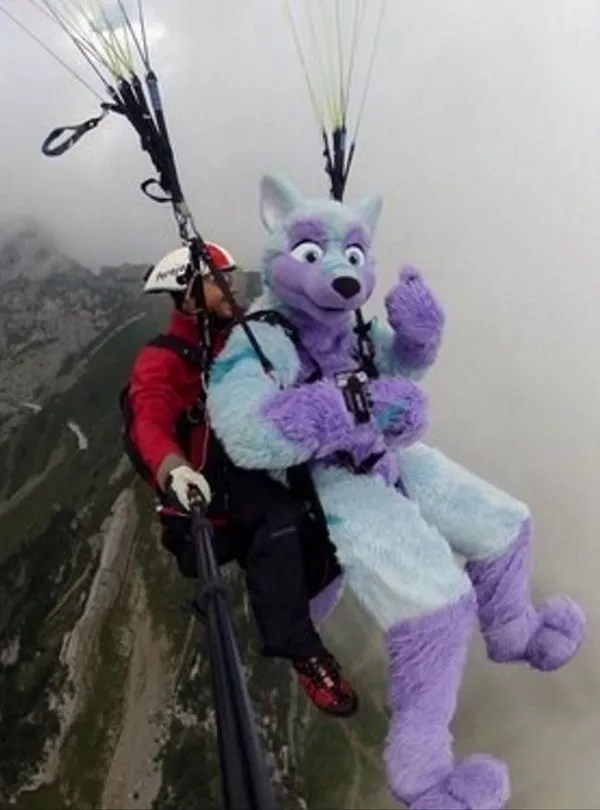Paragliding s postavou v kostýme zvieraťa v oblakoch nad horami.