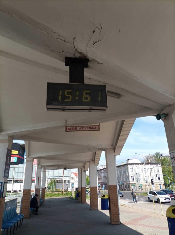 Elektronické hodiny na vlakovej stanici ukazujú nesprávny čas 15:61 pod upozornením: Palenie wzbronione.