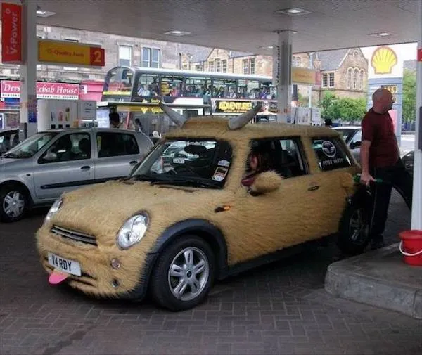 Mini Cooper upravené ako chlpatý býk, tankujúce na čerpacej stanici s človekom stojacim vedľa.