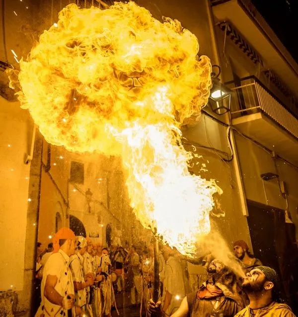 Ohnivá show na ulici počas festivalu; dav pozoruje muža vydychujúceho plamene do noci.
