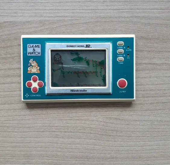 Starý prenosný herný konzol Nintendo Game & Watch s hrou Donkey Kong Jr. na drevenom povrchu.