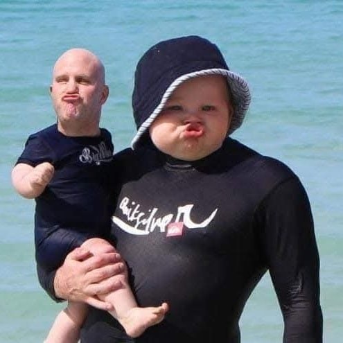 Dve osoby na pláži s premenenými hlavami, oblečené v plavkách, napodobňujú kačičkový výraz.