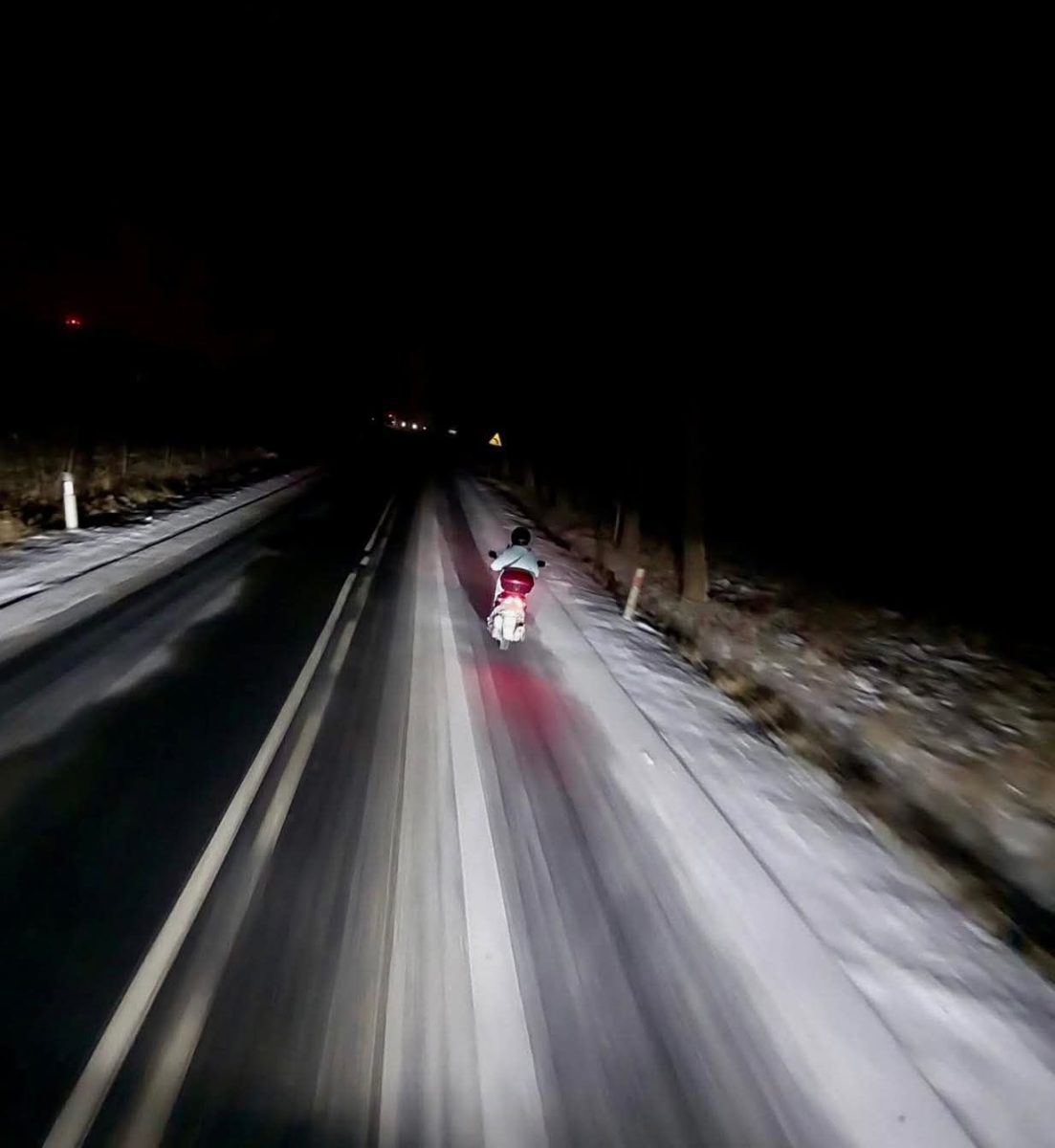 Motocyklista jazdí v noci po zasneženej ceste, osvetlené zadné svetlo skútra.