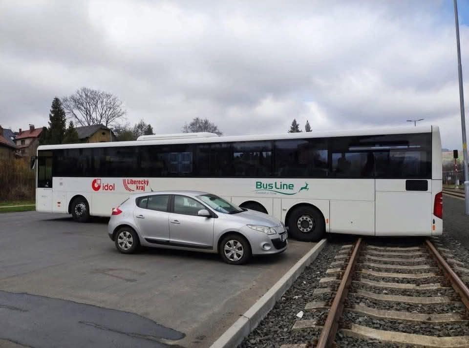 Osobné auto a autobus zablokujúci železničný prechod na križovatke, nútia vodičov k obchádzke.