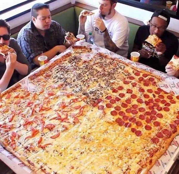 Ľudia si pochutnávajú na obrovskej pizzi s rôznymi príchuťami na obrovskom stole v reštaurácii.