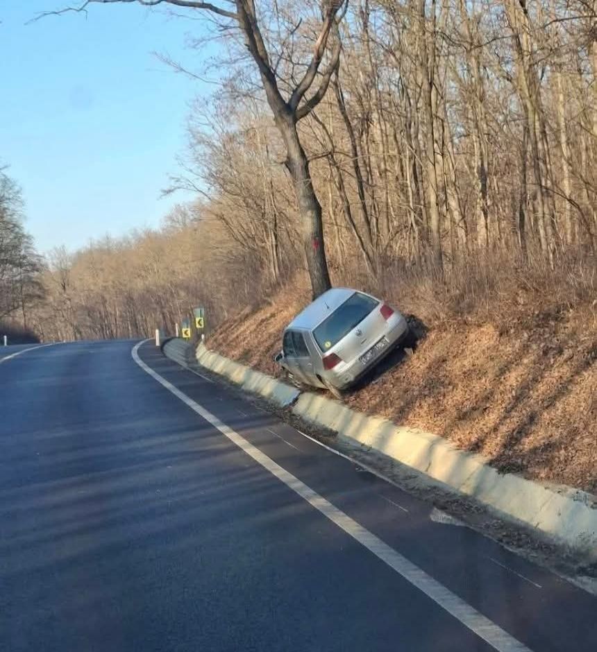 Auto zaparkované mimo cesty v priekop, suchý les v pozadí, jasný modrý deň.