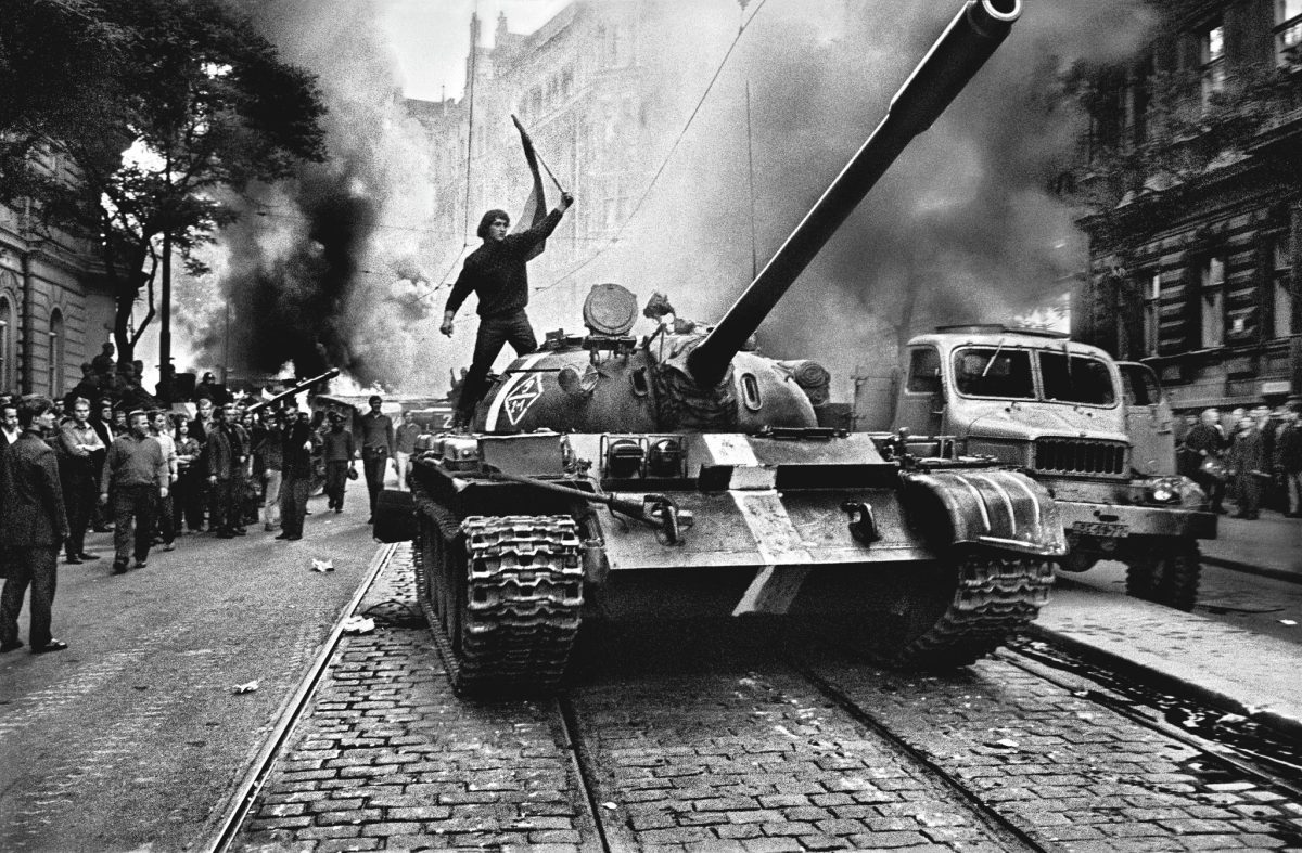Muž stojaci na tanku počas protestu v meste, obklopený dymom a davom ľudí na ulici.