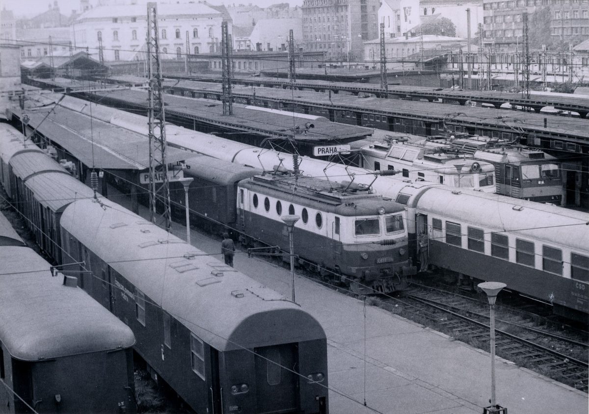 Historické nádražie s elektrickými vlakmi v Prahe, obklopené starými budovami.