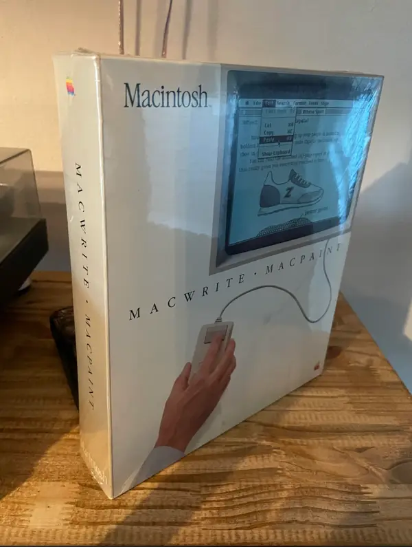 Krabica softvéru MacWrite a MacPaint pre Macintosh na drevenom stole.
