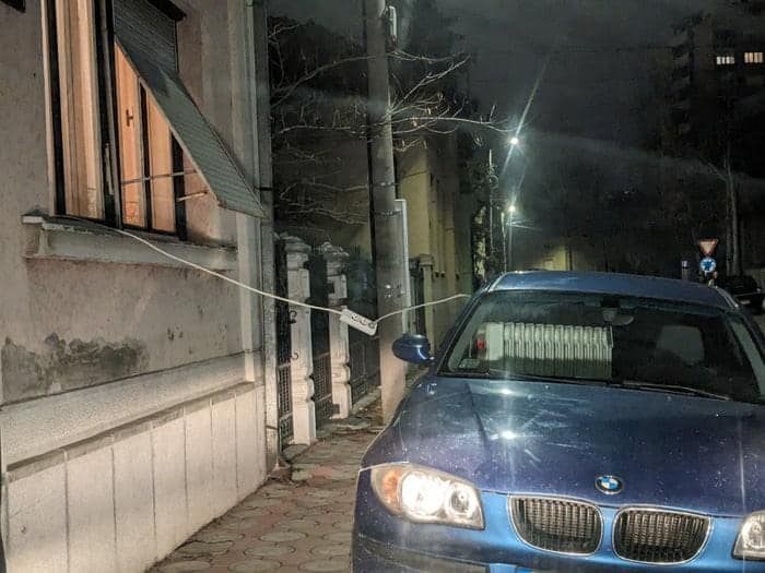 Auto parkujúce pri dome, nabíjané predlžovačkou cez okno, noc.